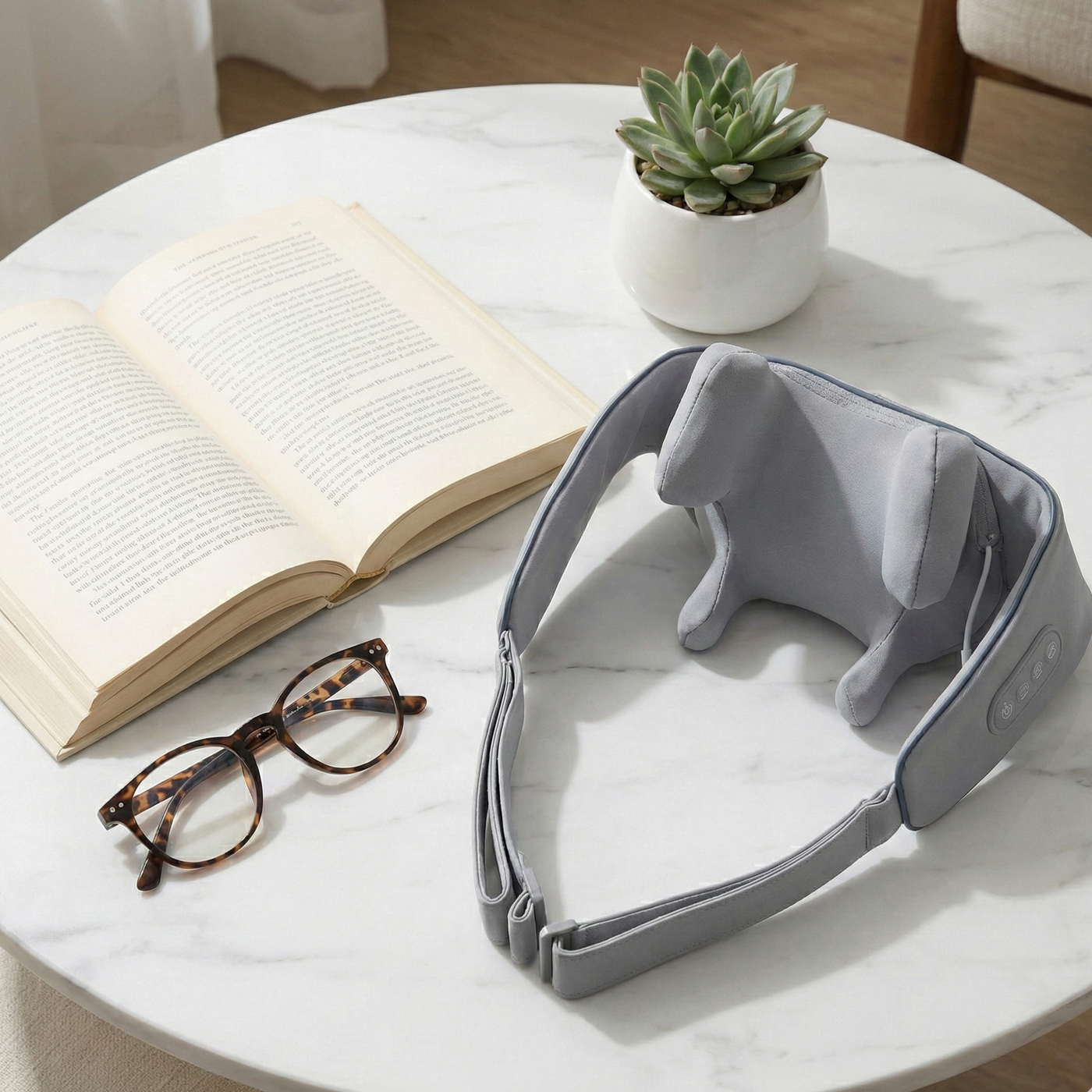 Gray neck massager on a marble table with an open book and glasses