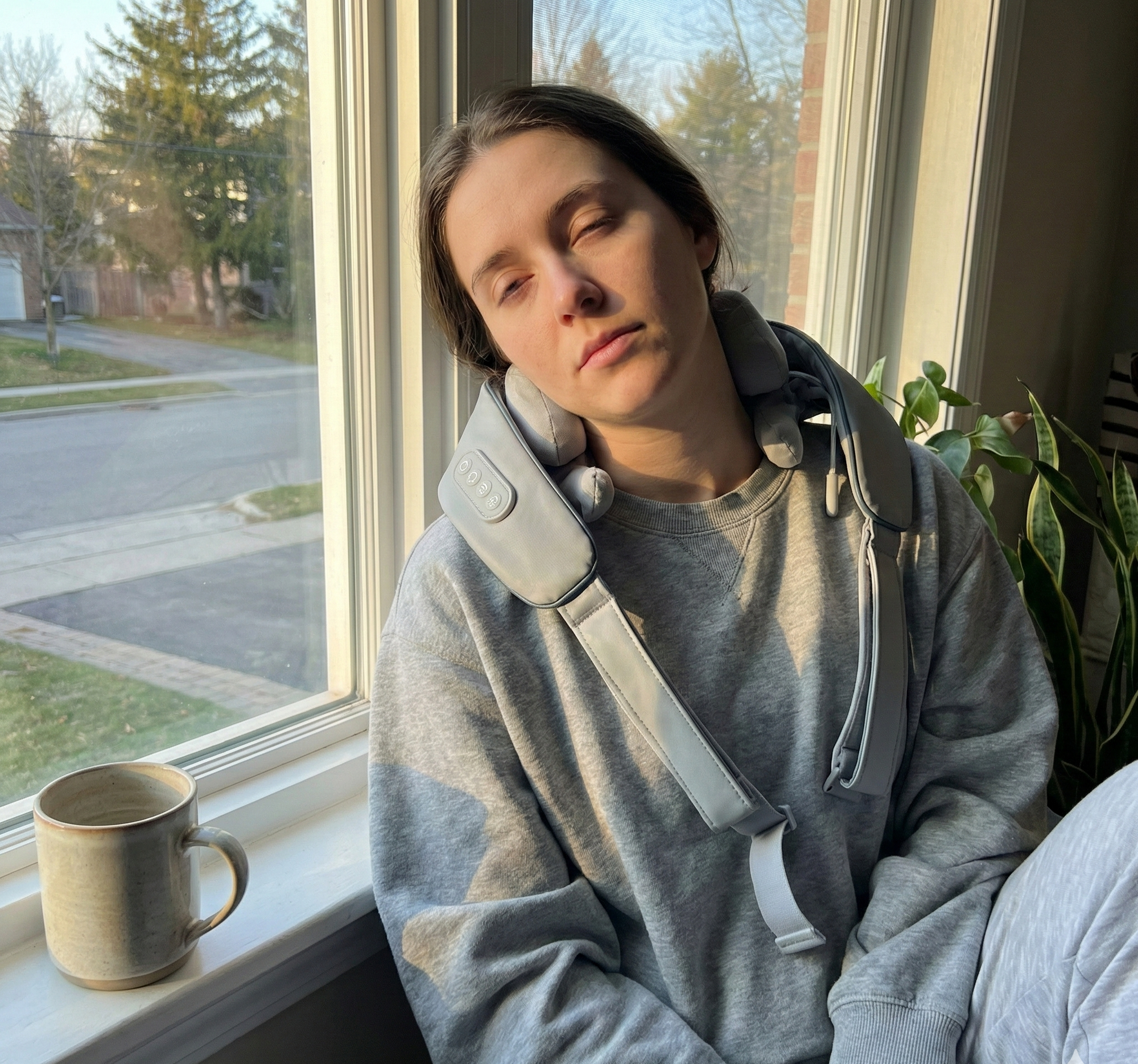 Person wearing a gray hoodie sitting by a window with a mug on the windowsill.